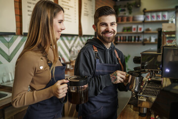 Two young smiling and pretty barista at work. Professional barista team brewing coffee using coffee machine in coffee shop