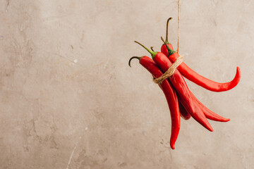 bunch of red chili peppers tied with rope hanging on beige concrete background - Powered by Adobe