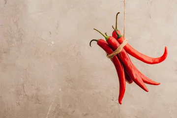 Tuinposter bunch of red chili peppers tied with rope hanging on beige concrete background © LIGHTFIELD STUDIOS