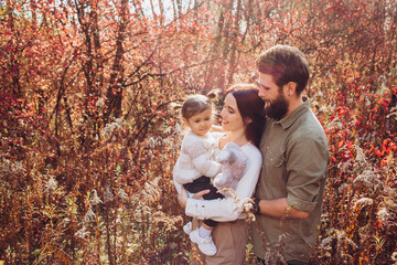 Young parents with daughter walk in autumn park, family portrait outdoors