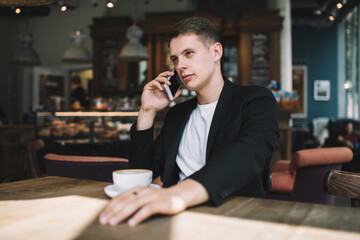 Serious young male speaking on smartphone in cafe