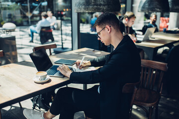 Concentrated man with laptop writing notes in cafe