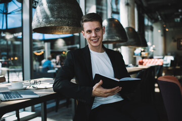 Young smart businessman taking notes in organizer in cafe