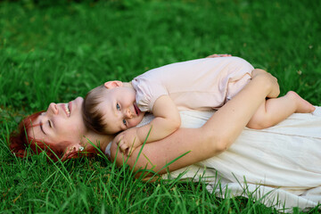 Mom and her one-year-old daughter are hugging on the grass in the park.
