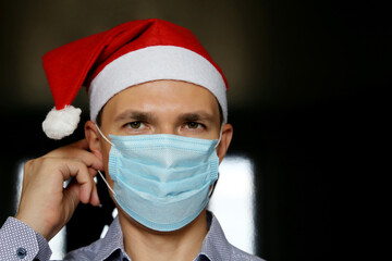 Portrait of man in medical face mask and Santa Claus hat. Christmas celebration during coronavirus pandemic