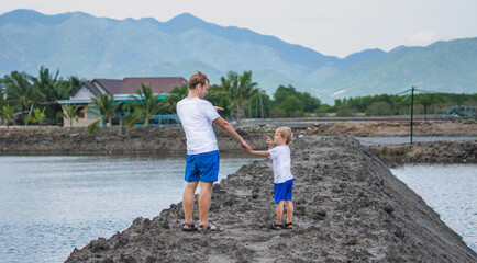 Father son walk near mountain lake, look point at each other, winking playing. Happy childhood....