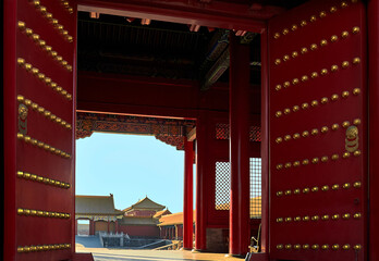 view through an ancient red gate with gold decorations to the square with historical buildings. The...