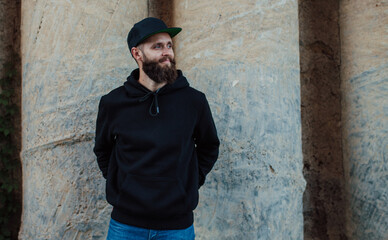 Fototapeta premium City portrait of handsome hipster guy with beard wearing black blank hoodie or sweatshirt with space for your logo or design. Mockup for print