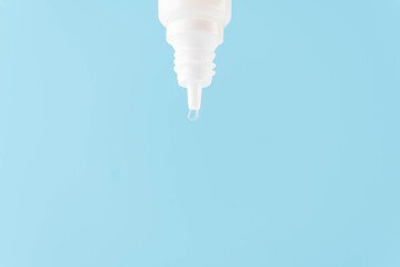 Eye drop or ear drop bottle with droplet on blue background. Pharmaceutical product. Copy space.