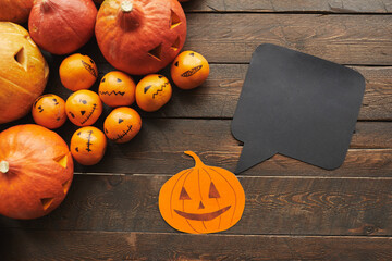 Horizontal top-down shot of carved pumpkins, tangerines paper Jack-O'-Lantern with black quote box lying on dark brown wooden table - Powered by Adobe
