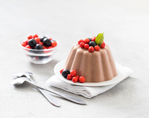 Chocolate pudding with fresh berries black and red currants on a plate on a light background