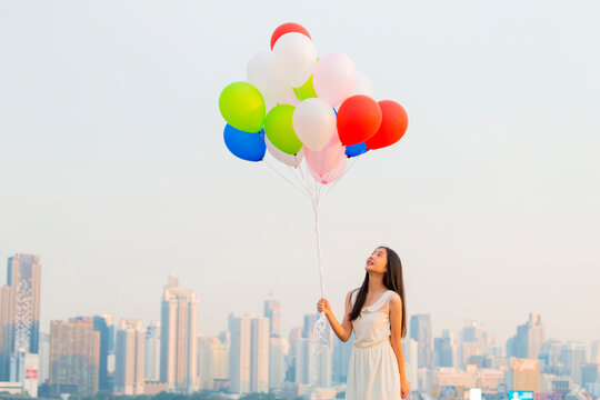Follow your dream, Inspiration Concept - Young woman with colorful balloons having fun on rooftop balcony with cityscape at sunset. Fun, Vacation, Bright life