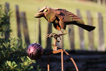 A Christmas bauble suspended from a metal crow in a winter garden.