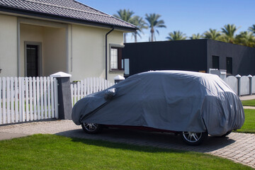 Car is parked under a canopy on a lawn with a house and palm trees in the background.