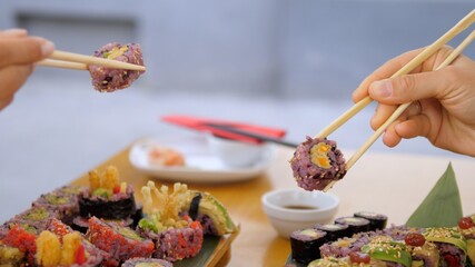 Sushi dinner. Side view of two hands picking up sushi rolls with chopsticks. Artisan Asian cuisine