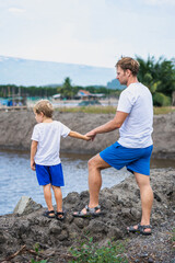 Father and son walk along man made breeding fish lake mountain background. Happy childhood. Home...