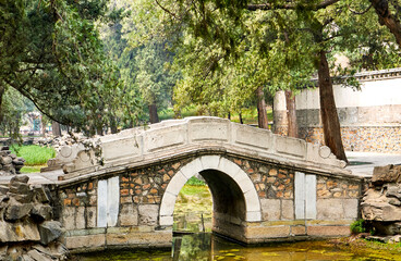 Fototapeta na wymiar Ancient stone bridge surrounded by ancient trees in the Imperial Summer Palace park. Beijing, China