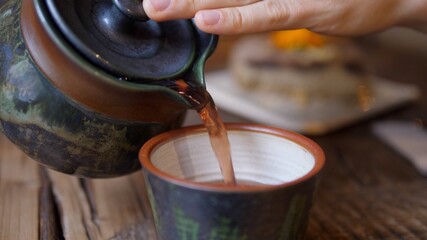 Tea ceremony. Pouring black tea from tea kettle to the mug.