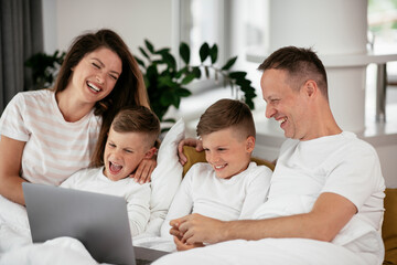 Beautiful parents with kids enjoying at home. Young family watching movie on lap top..