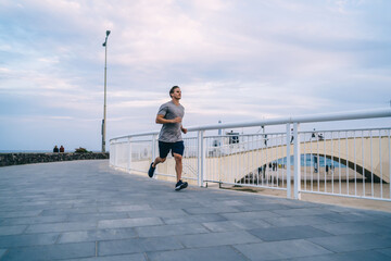 Happy young male jogger in active clothes reaching running goals on cardio workout in morning, slim...