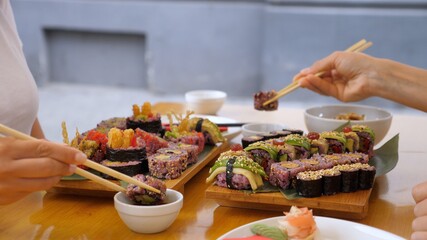 Two people dipping sushi rolls into soy sauce and eating it. Heathy Asian street food
