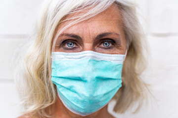 Life during the Covid-19 epidemic. Gray-haired european woman wearing  cyan protective mask looking at the camera