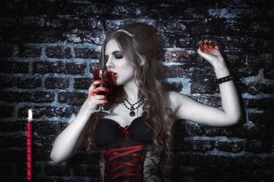 A vampire woman looks at a bloody flower. A glass of blood. Brick wall. 
