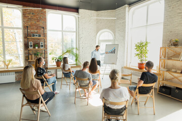 Male speaker giving presentation in hall at university workshop. Audience or conference hall. Young students, participants in audience wearing face mask. Scientific conference event, training