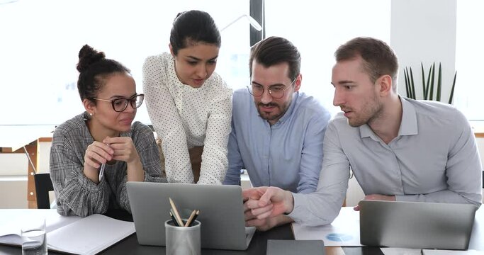 Multi ethnic colleagues staff members gather in modern office boardroom using computer discussing common project, make analysis of work done sales statistics and forecasting. Teamwork activity concept