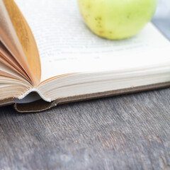 An open book on an old wooden background.  The green Apple is on the page of the book.