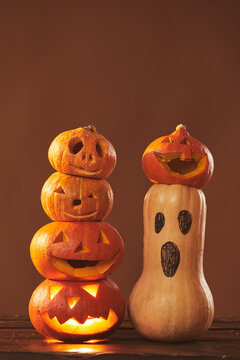 Still life composition studio shot of ripe pumpkins carved and gourd painted for Halloween party decoration, brown background