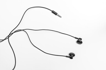 Small black headphones on a light background with tangled long wires