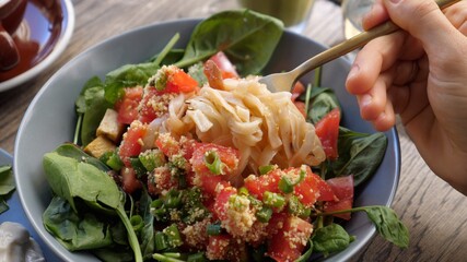 Close up of fork picking up noodles from colorful warm salad bowl with spinach and tomato. Healthy...