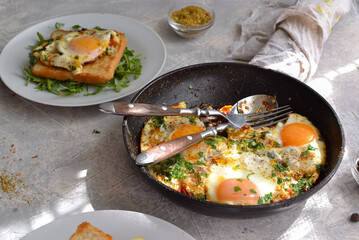 fried eggs with tomatoes, onions and parsley in a pan. Toast with cheese and sausage. Tasty breakfast. Light background. Shakshuka.