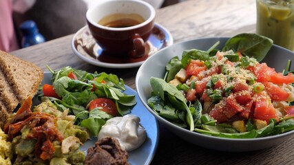 Healthy vegan brunch in the city. Close up of full English breakfast, salad with spinach, coffee and matcha ice tea latte. 