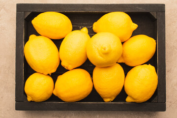 top view of ripe yellow lemons win wooden box on beige concrete surface