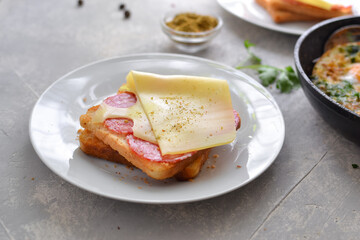 Delicious fast food breakfast. Crispy Toast with cheese and sausage. Sandwich in a white plate Light background. Minimalistic food photo. Close up