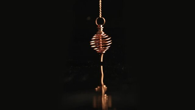 Golden energy pendulum in the form of a spiral swings against a black background
