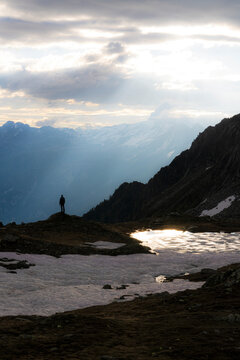 Silhouette of man standing under sun rays at dawn on shores of lake Zana, Valmalenco, Valtellina, Lombardy