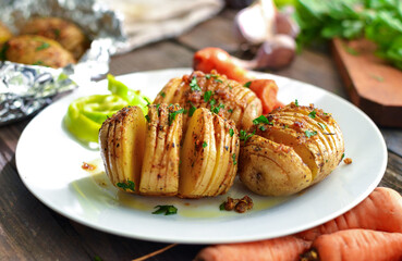 Baked potatoes with carrots. White plate. Wooden background. Delicious and healthy lunch. Hasselback potatoes. Close up