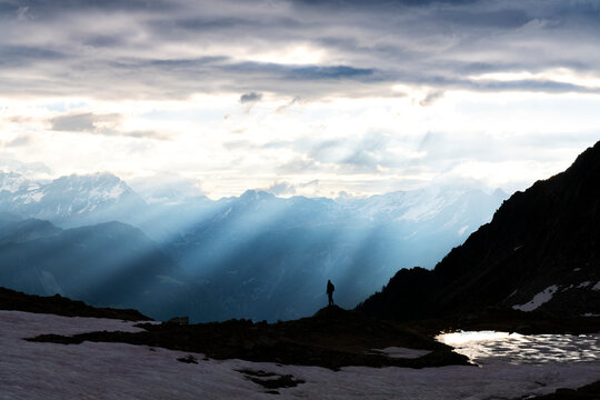 Silhouette of lone hiker admiring the sun rays at dawn over lake Zana, Valmalenco, Valtellina, Lombardy