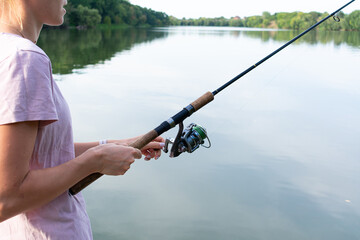 Cute woman is fishing with rod on the summer lake. Woman fishes on the river