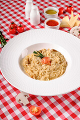 Flat lay. Creamy risotto with cherry tomatoes, rosemary and mushrooms in porcelain plate. Rustic style in italian restaurant background, top view. Italy food. Close up