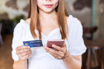 Young woman holding a credit card and using smartphone for making online payment shopping in restaurant