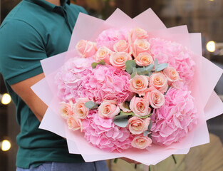 Man with bunch of pink hydrangea and roses. Young man holding a big bouquet of pink  flowers in Women's day. Fresh cut flowers.