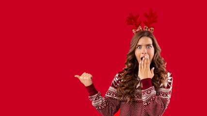 Christmas sale. Shocked millennial woman pointing at blank space over red background