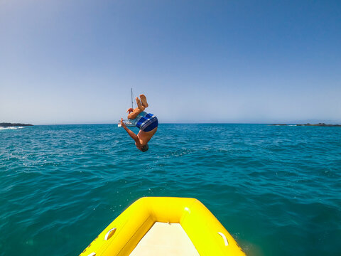 Teenager and young man jump and doing a backflip in the boat or dinghy to the water having fun and enjoying summer vacations in the ocean - caucasian people at the beach renting a boat