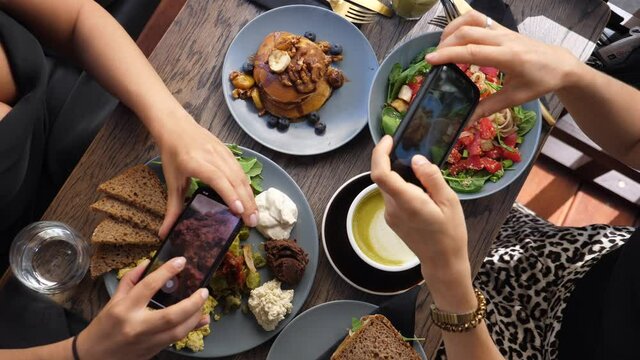 Top view of hands of two people taking pictures of a colorful healthy brunch 