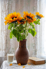 A bright bouquet of sunflowers in a clay jug on the background of a lace curtain.
