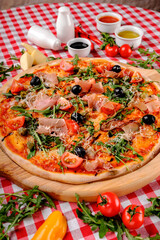 Rustic pizza with jamon, fresh arugula, cherry tomatoes, balsamic vinegar, black olives and tomatoes sauce in italian restaurant background, top view. Italy food. Close up